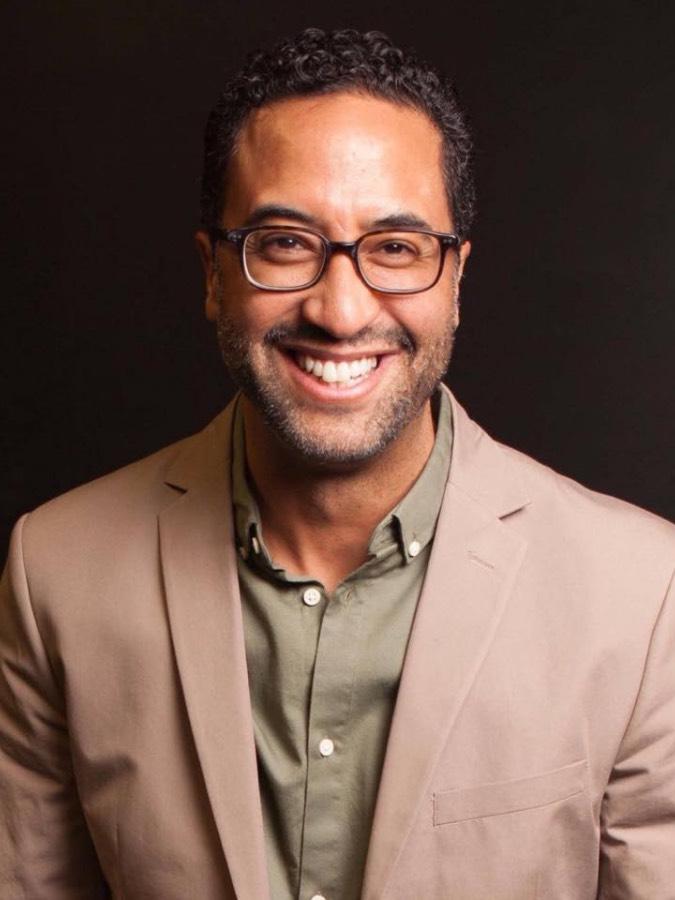 A man wearing glasses and shown from the shoulders up smiles.