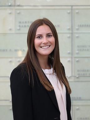 A young woman with brown hair stands with her arms crossed in a suit jacket for a professional image.