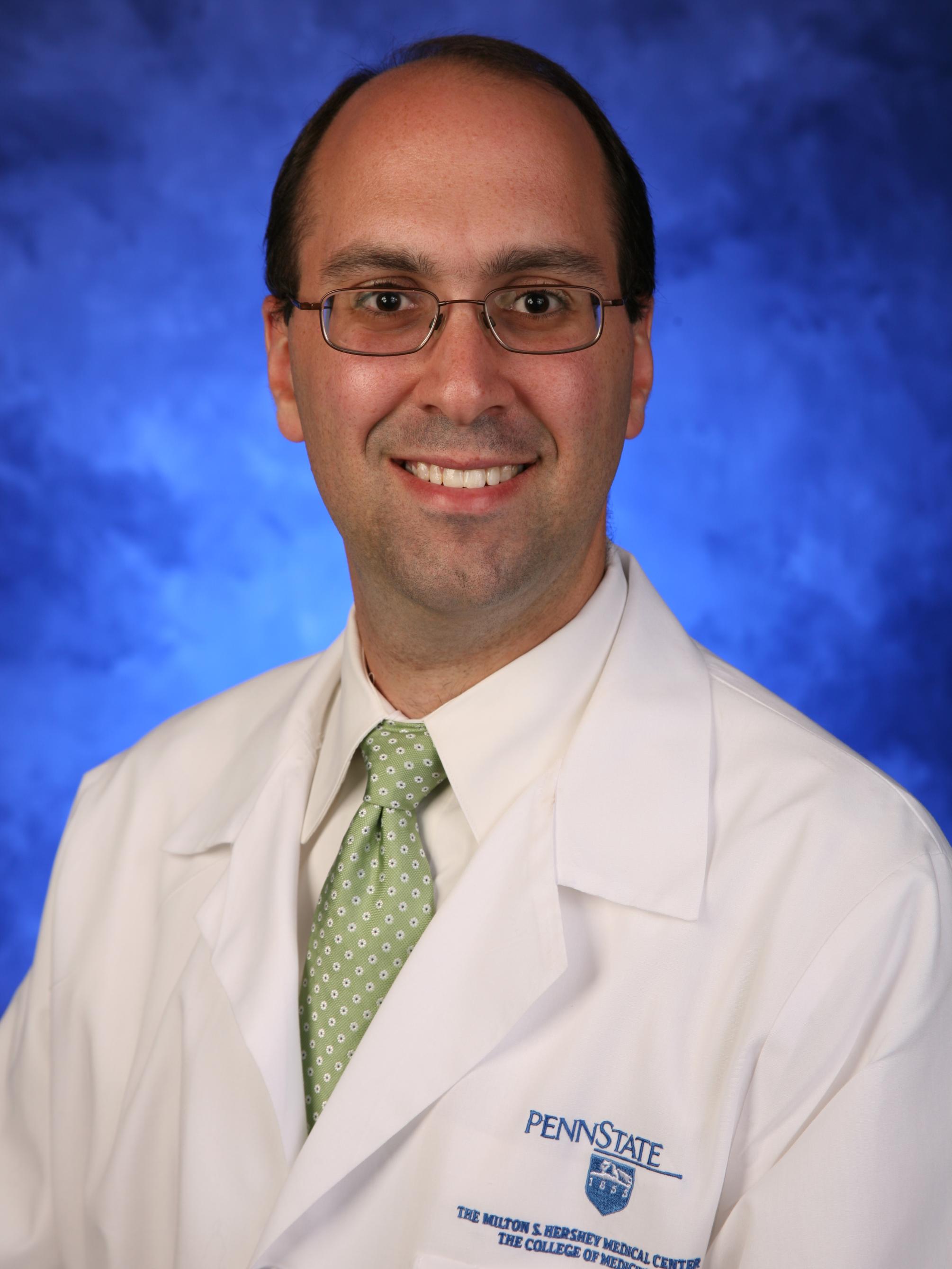 Dr. Brian Saunders poses for a professional photo wearing a tie and a physician's coat bearing the Milton S. Hershey Medical Center logo.
