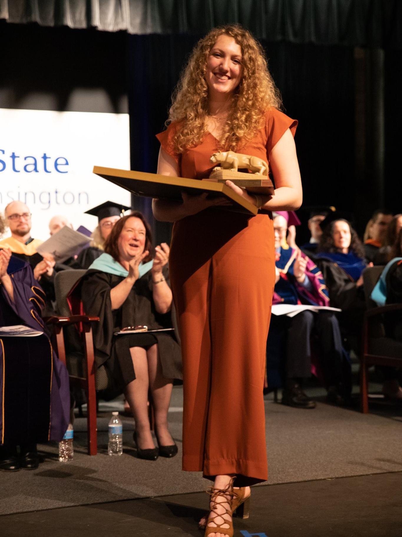Female student stands on stage holding award