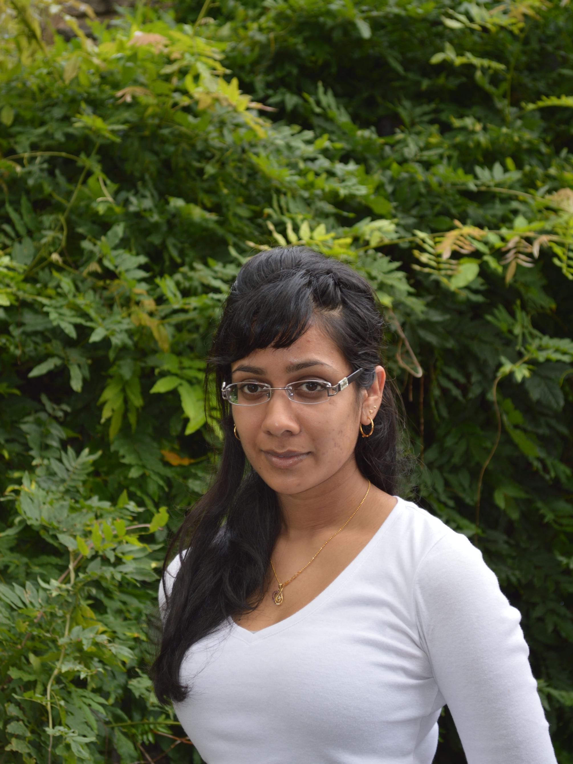 vertical photo of woman Nari Senanayake standing outside in front of lush green shrubs