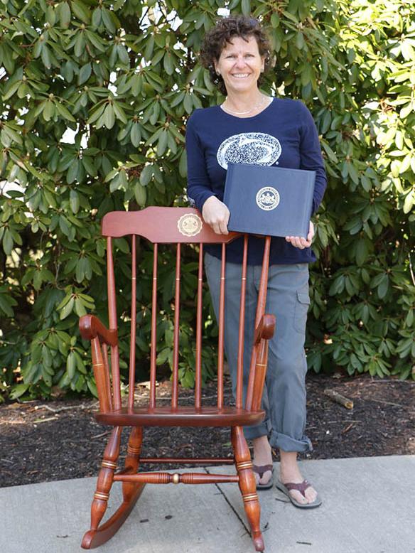 Woman standing in front of rocking chair holding a certificate.