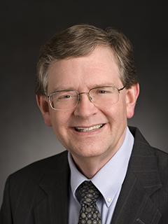 Head shot of a man with glasses wearing a suit and tie