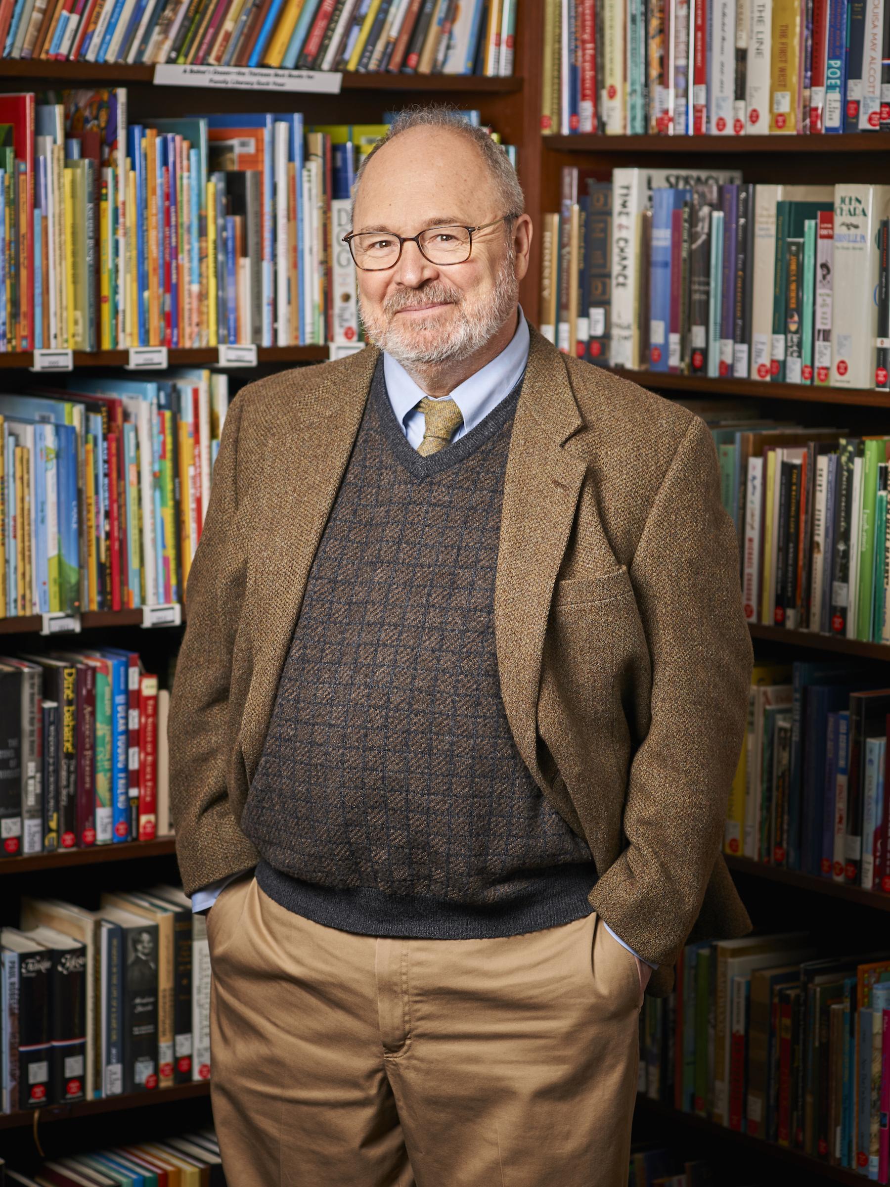 photo of man standing in front of corner bookshelves full of children's books