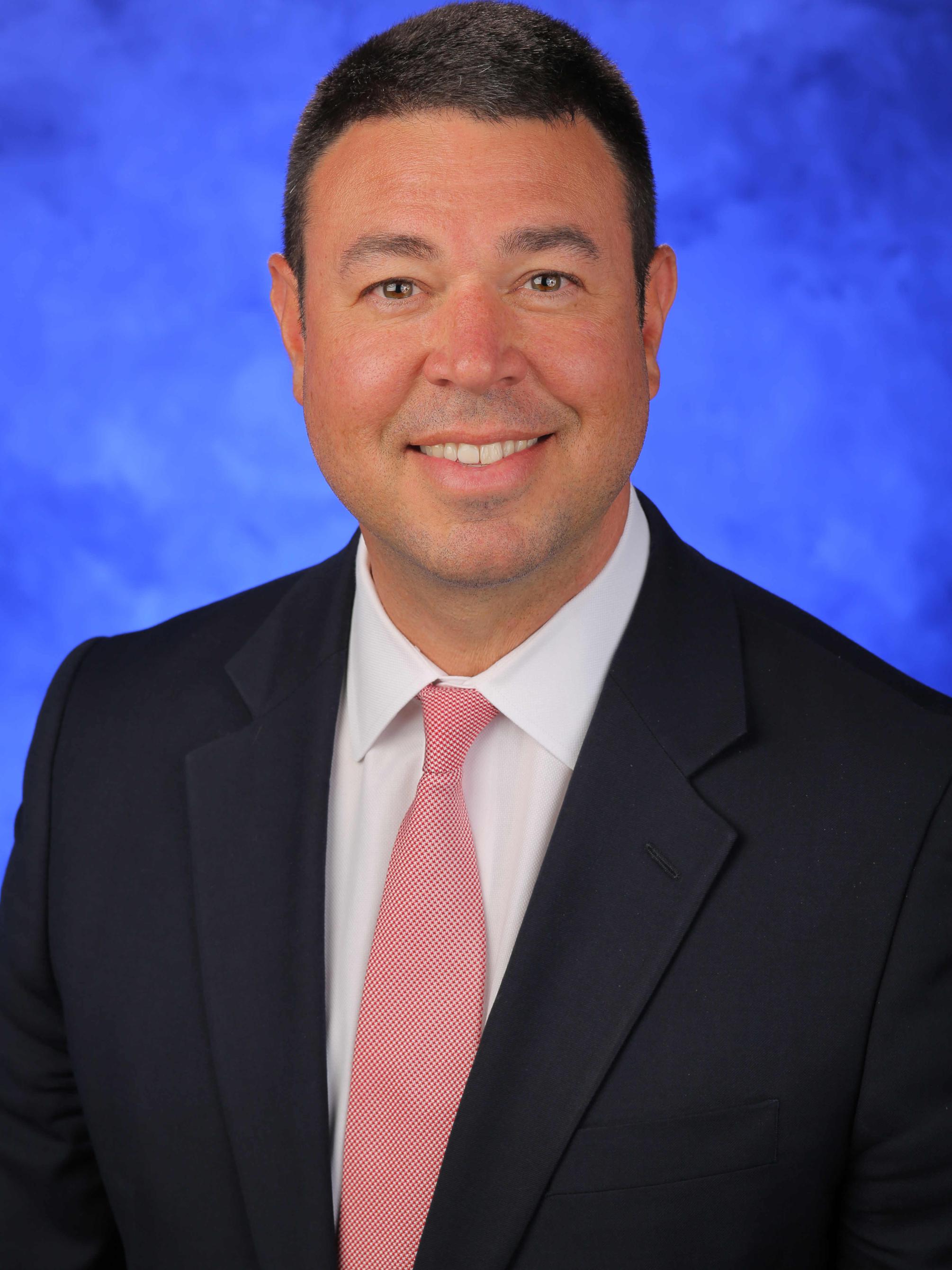 Tom Stoessel poses for a professional headshot, wearing a suit.