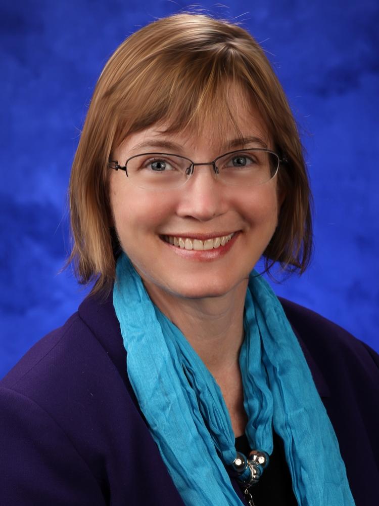 Heather Stuckey, wearing a dark blouse, scarf and necklace, poses for a professional headshot photo.