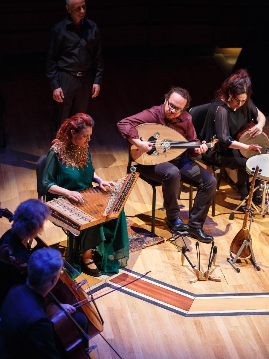 Musicians sit in chairs on a stage and play their Baroque-period instruments.