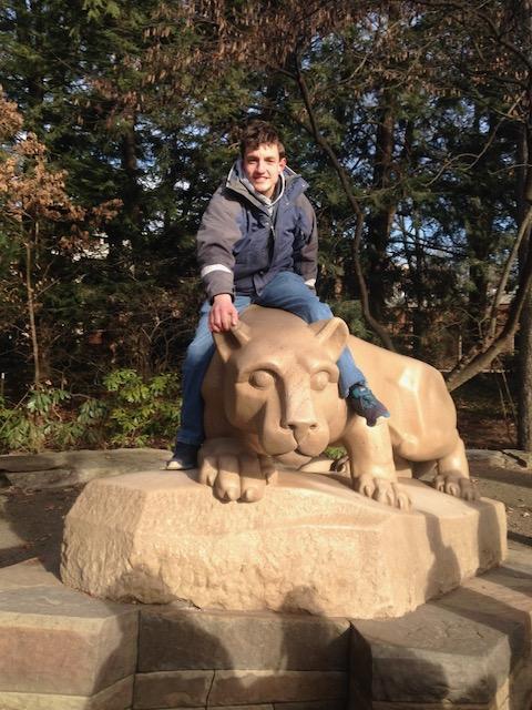 A young man in a winter jacket sits on the Penn State Lion Shrine.