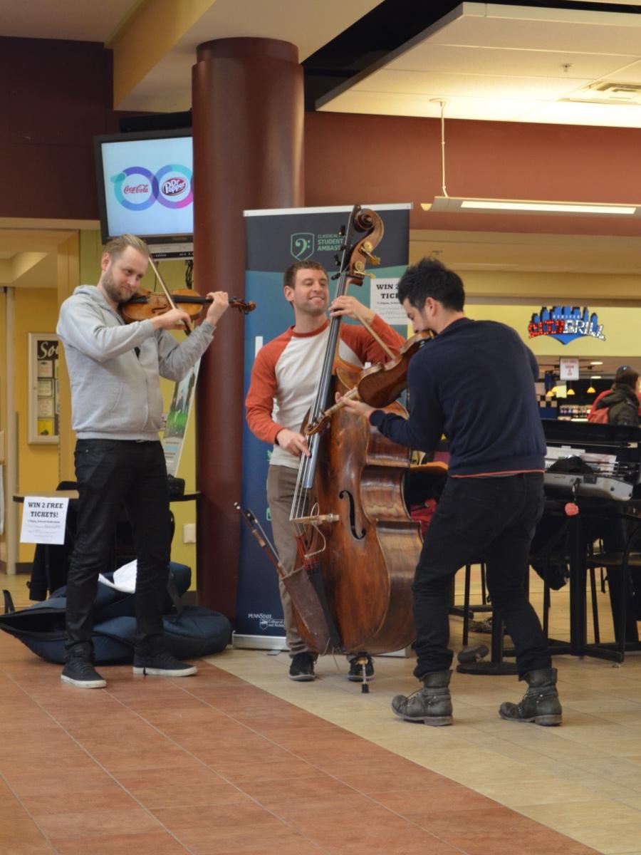 Three string musicians smile while they perform in a cafeteria.