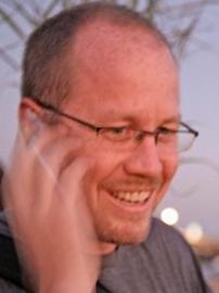 A man wearing glasses has his hand up to his ear.
