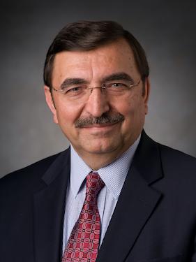 A professor wearing glasses and a suit and tie poses for a professional headshot.