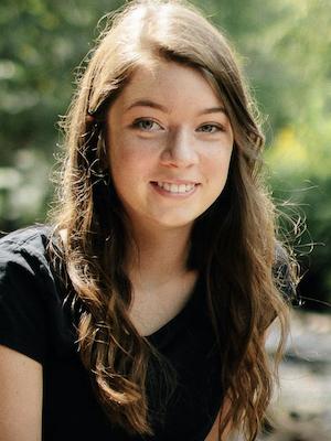 A young woman with long brown hair smiles on a sunny day. 