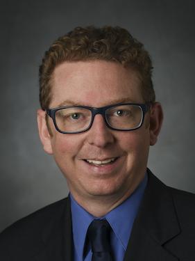 A professor smiles for a professional headshot.