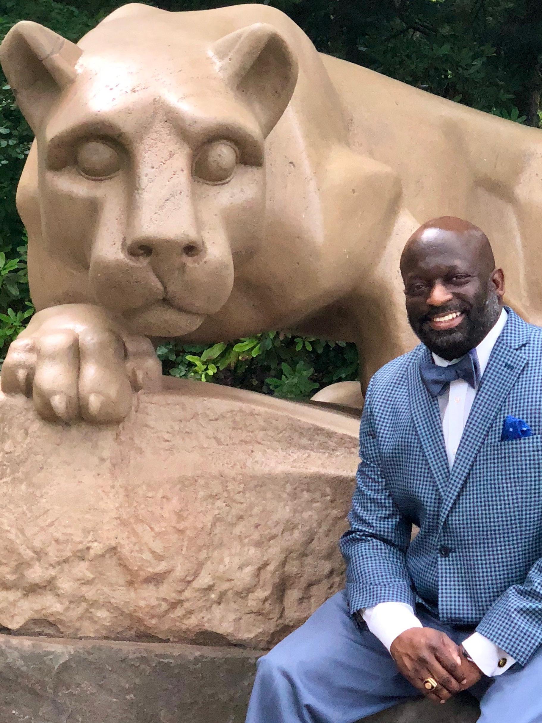man sitting next to the Nittany lion shrine at university park 