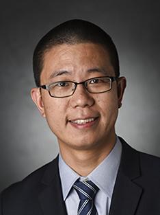 Headshot of a man wearing glasses, a light blue shirt, suit jacket and tie