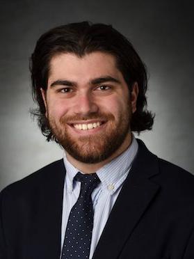 male in professional attire with dark hair smiles and poses for professional photo