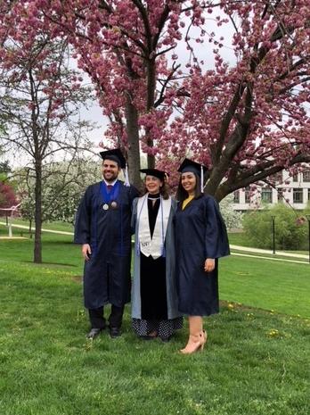 Professor posing with two students under tree in caps and gowns