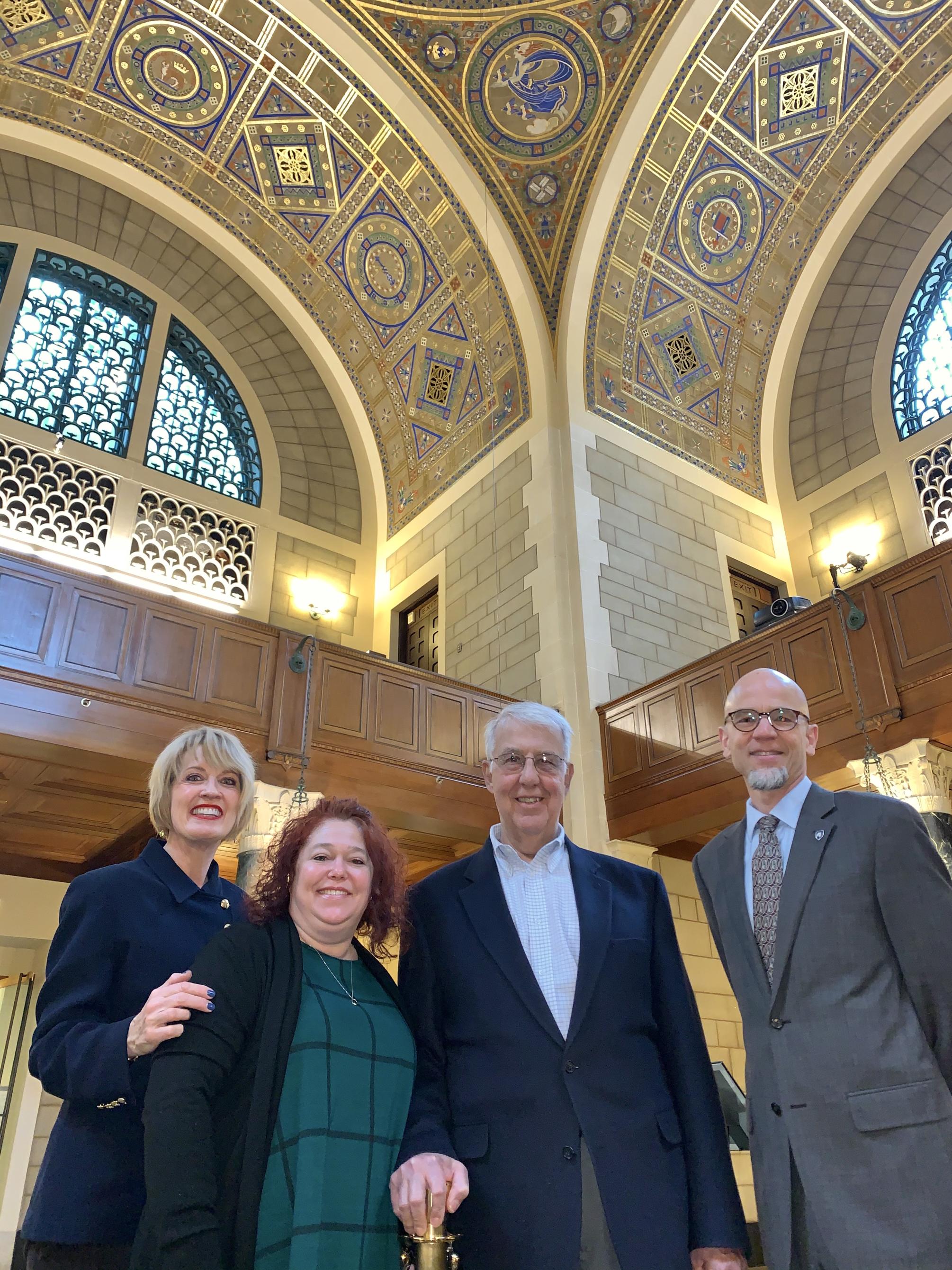 four people with decorative ceiling behind them