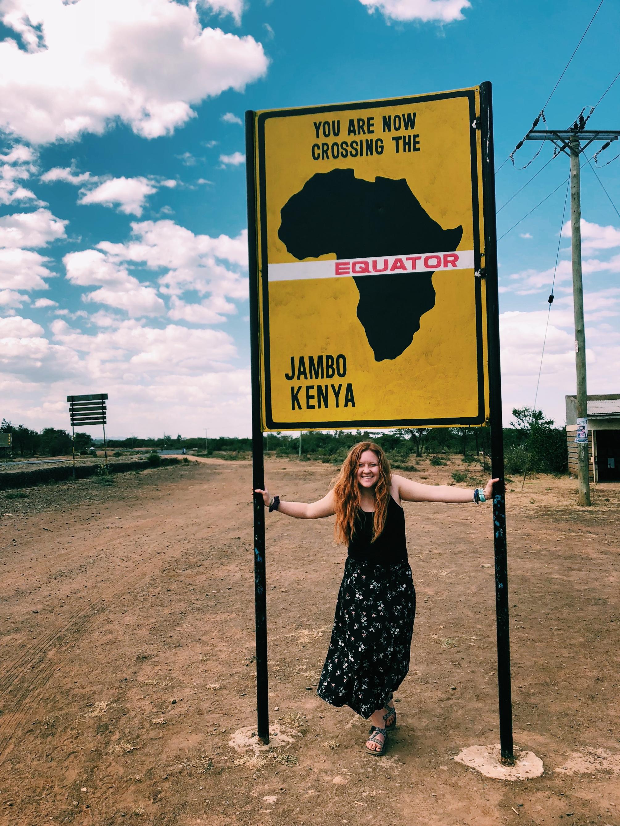 A young woman under a sign that reads, "You are now crossing the equator"