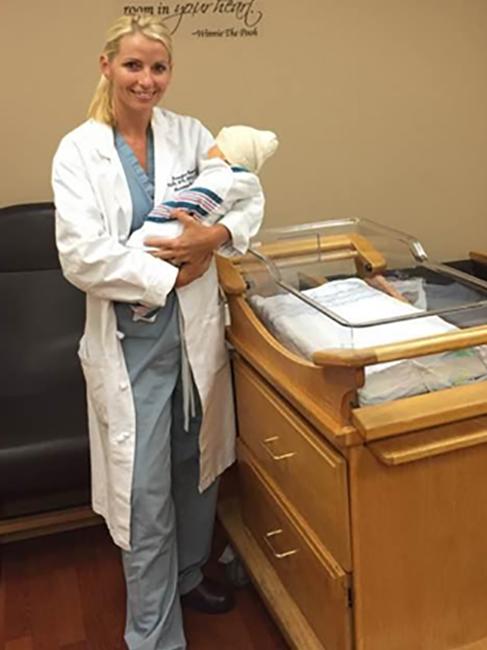 Photo of Jennifer Kelly-Connolly in her nursing scrubs holding an infant