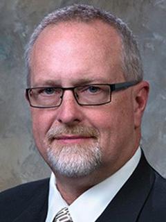 headshot of a man wearing a suit and glasses