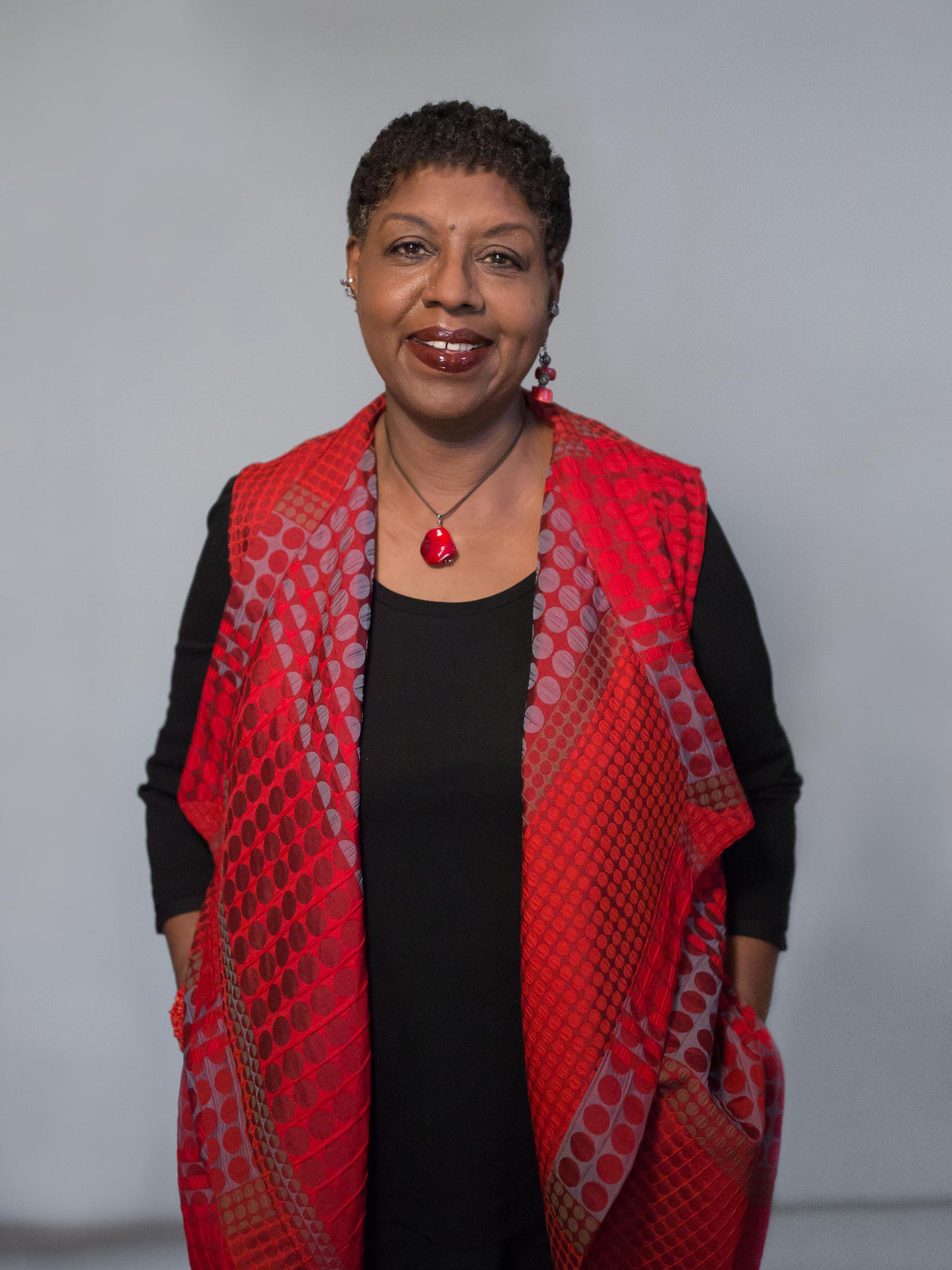 vertical photo portrait of woman standing with hands in pockets, wearing black clothes and bright red long scarf or vest with red stone necklace