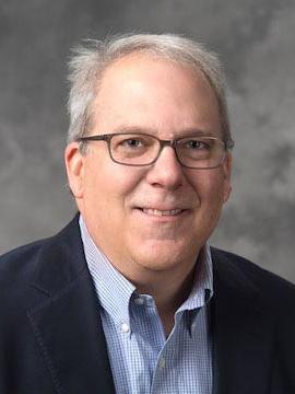 Paul Griffin headshot in black jacket, blue shirt, and glasses.