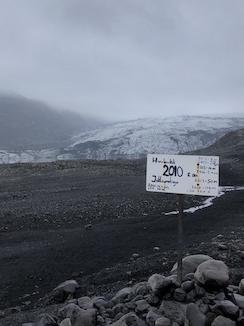 Image of glacier in background and bare ground in foreground with sign recording rate of receding 