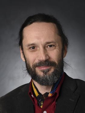 A professor wearing a black jacket and red shirt poses for a professional headshot.
