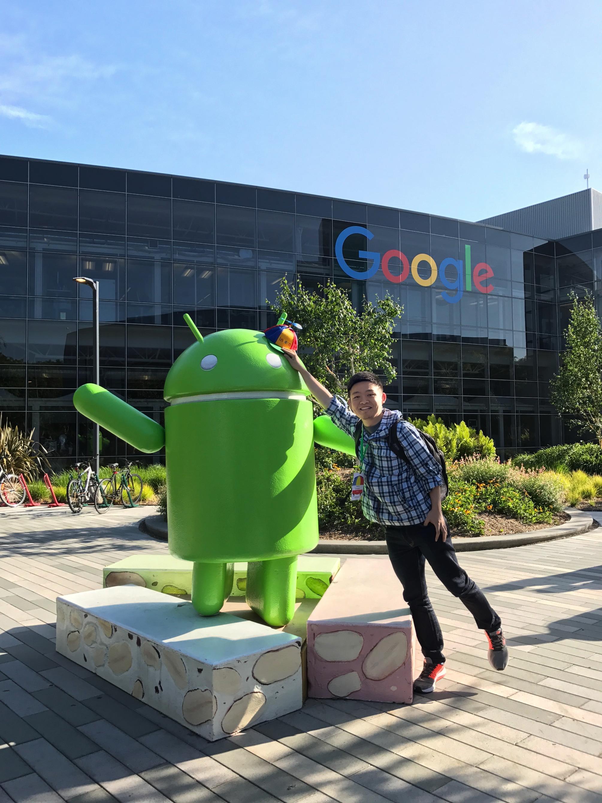 Geography Ph.D. student Xi Liu stands next to a statue of Google's Android mascot.