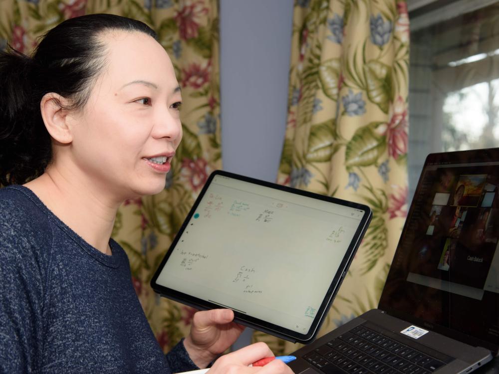 Woman holding iPad while video conferencing on a laptop with students