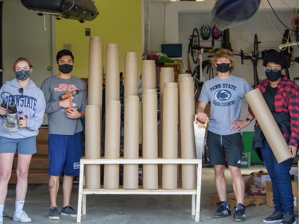 Four Penn State Behrend students pose next to a thongophone, a custom-built intstrument they constructed from used cardboard tubes.