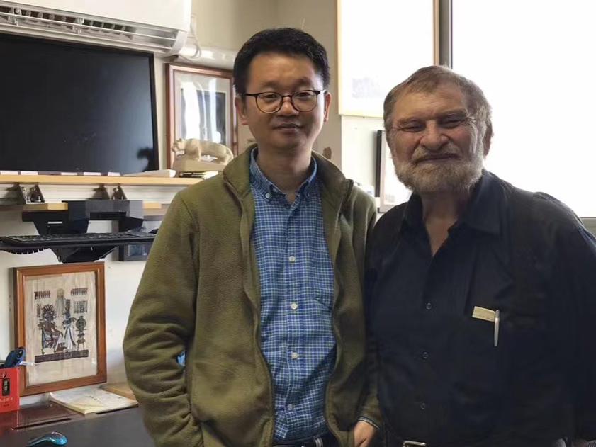 Two men stand together behind a desk in an office.