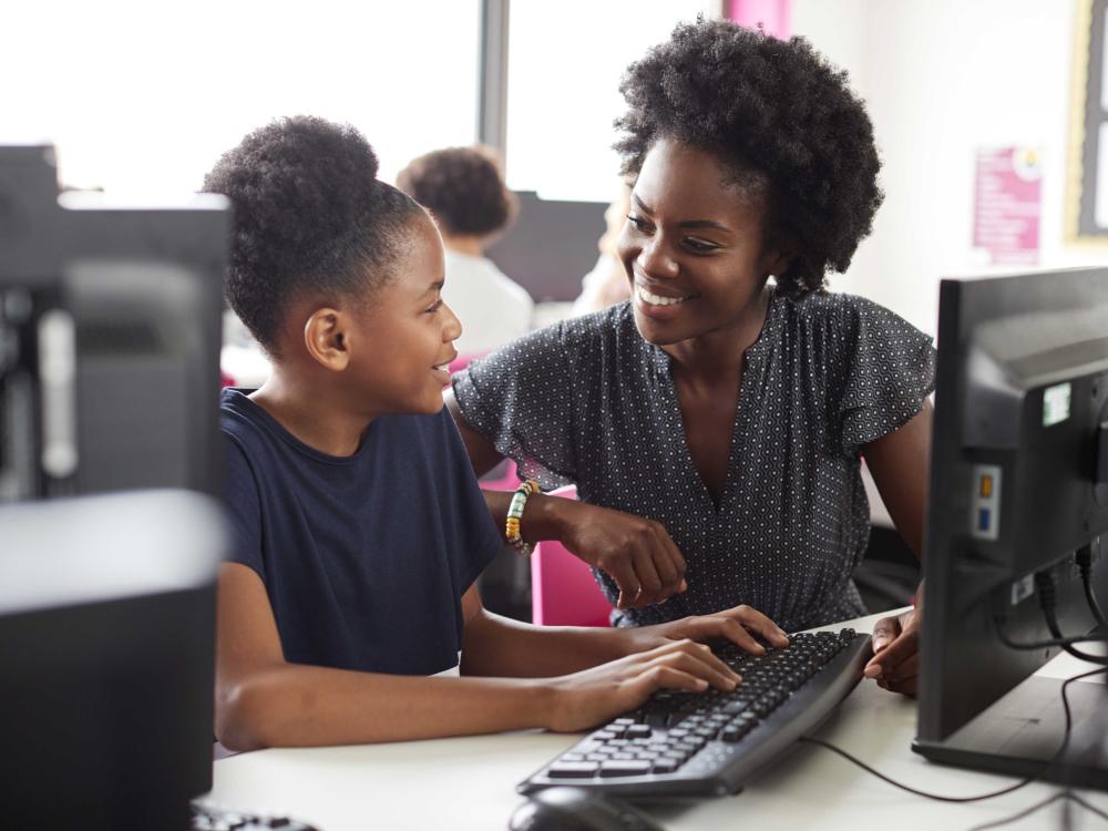 Teacher and teen student smiling in front of computer in school