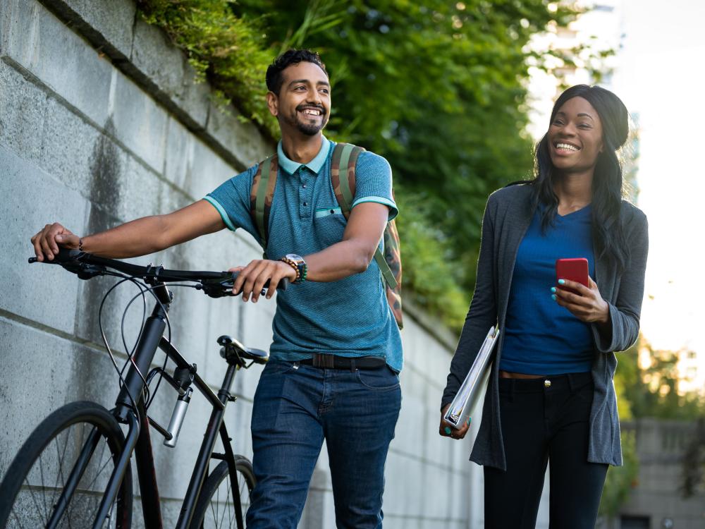 Young man pushing bike walking next two young woman carrying a binder and a smartphone