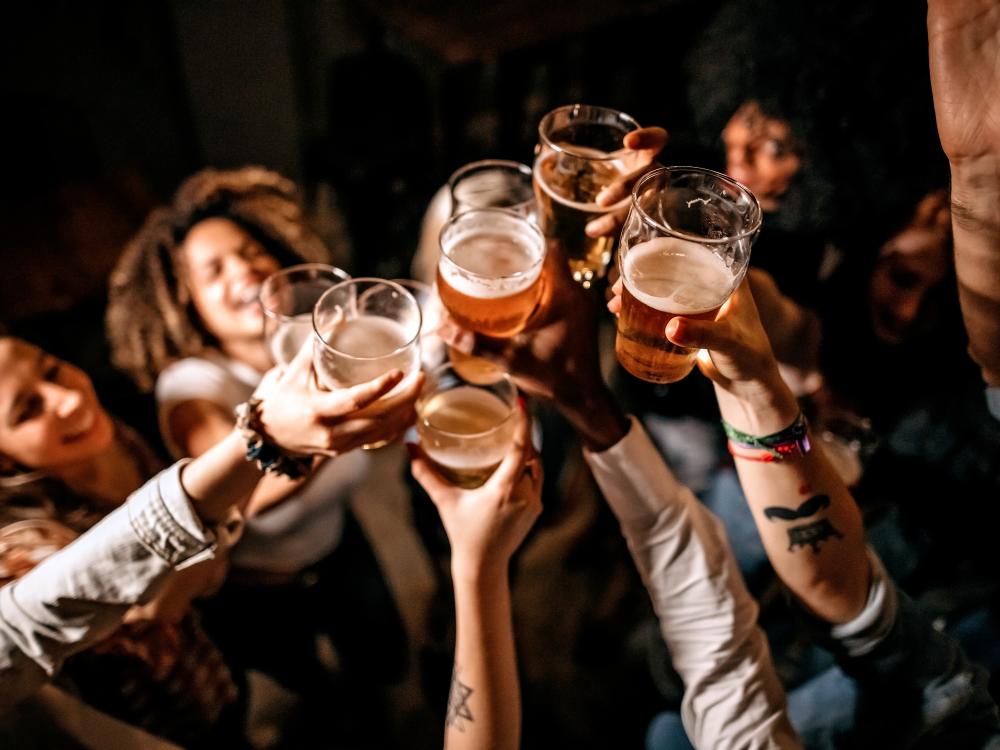 Several people in a dark room raising beer glasses for a toast