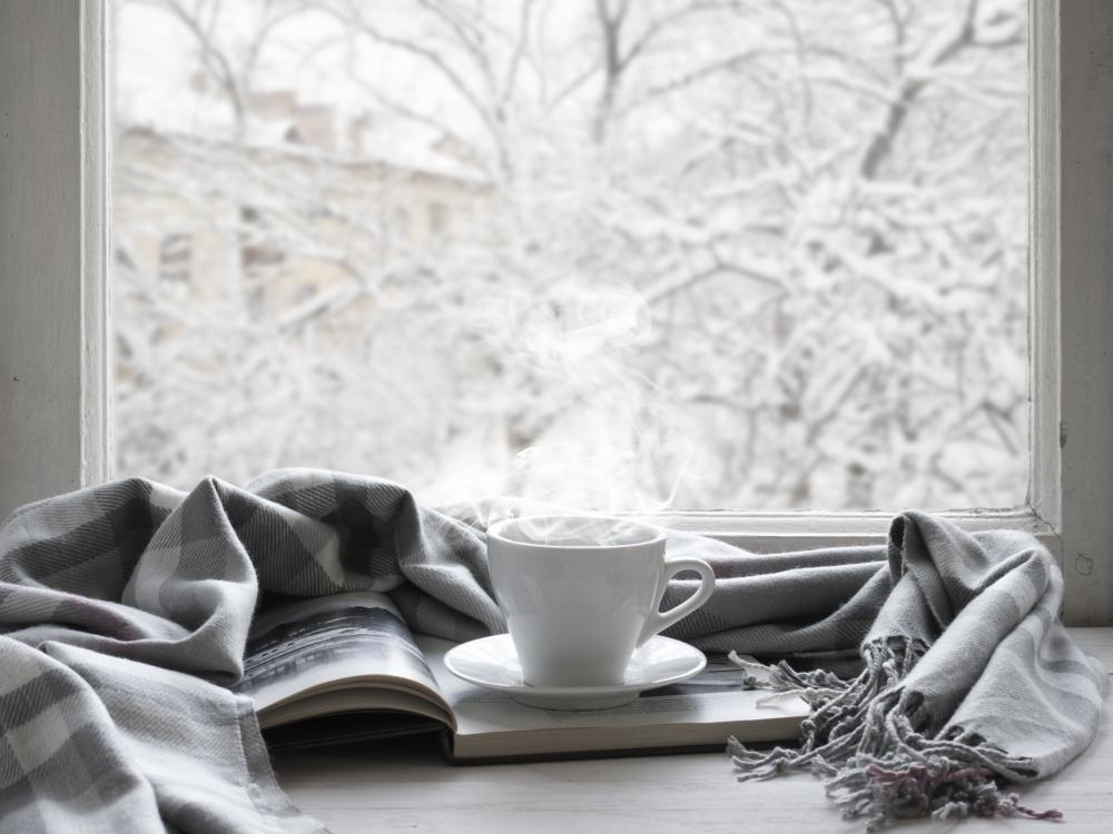 Photo of steaming mug sitting on desk in front of window showing snowy tree branches