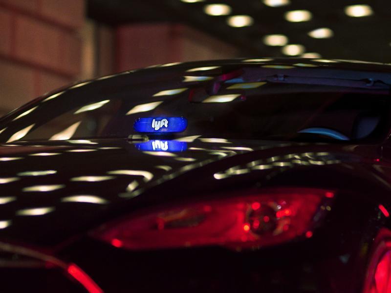 A black car driving at night with a Lyft sign illuminated in the front window