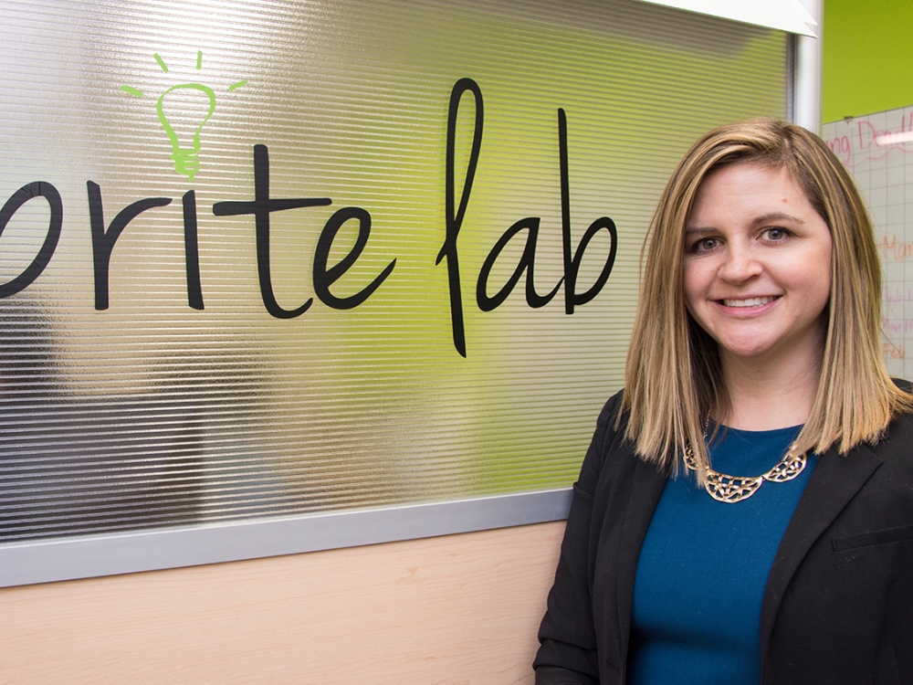 Person wearing a black blazer stands next to a sign that reads Brite Lab