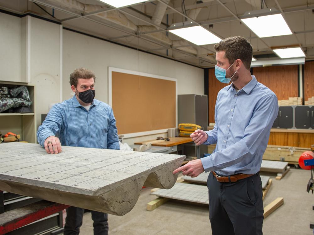 Two people wearing blue button-down shirts standing beside a scale concrete slab that has been raised off the floor.