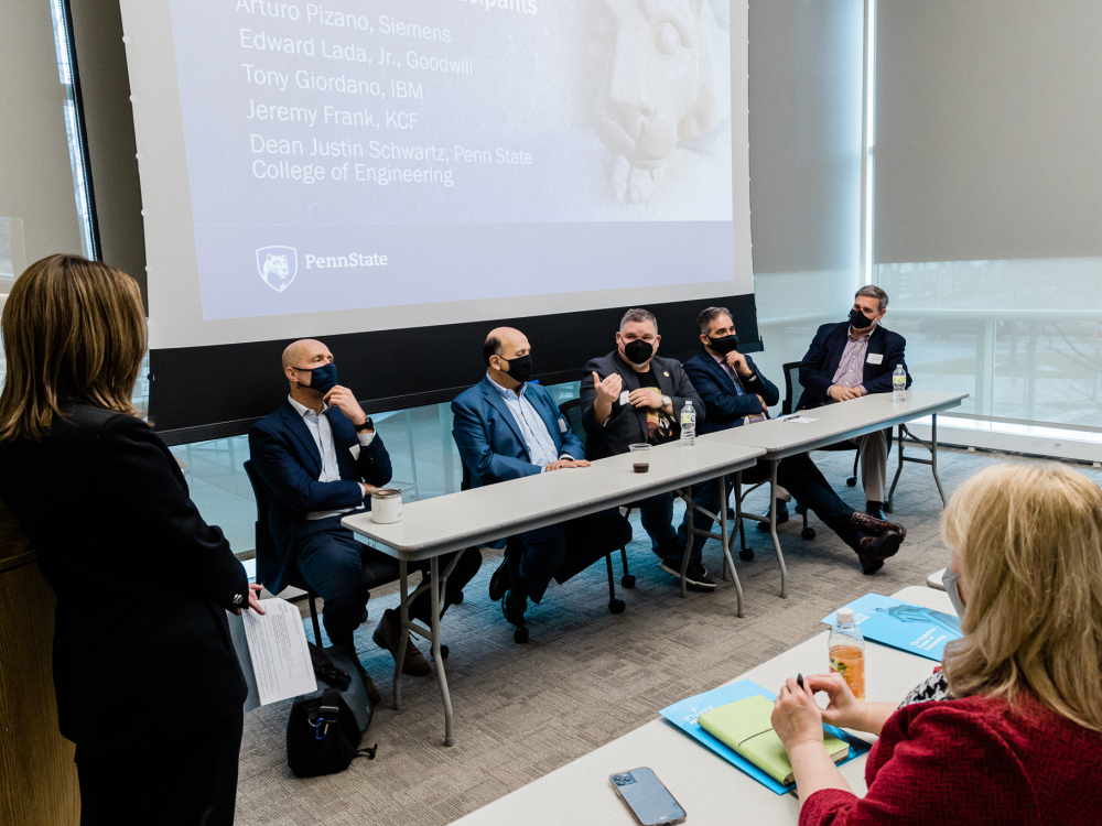 Fireside Chat panel takes place during summit with five people seated at a table in front of a conference audience