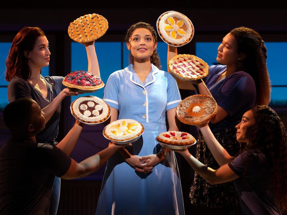A woman stands surrounded by baked pies.