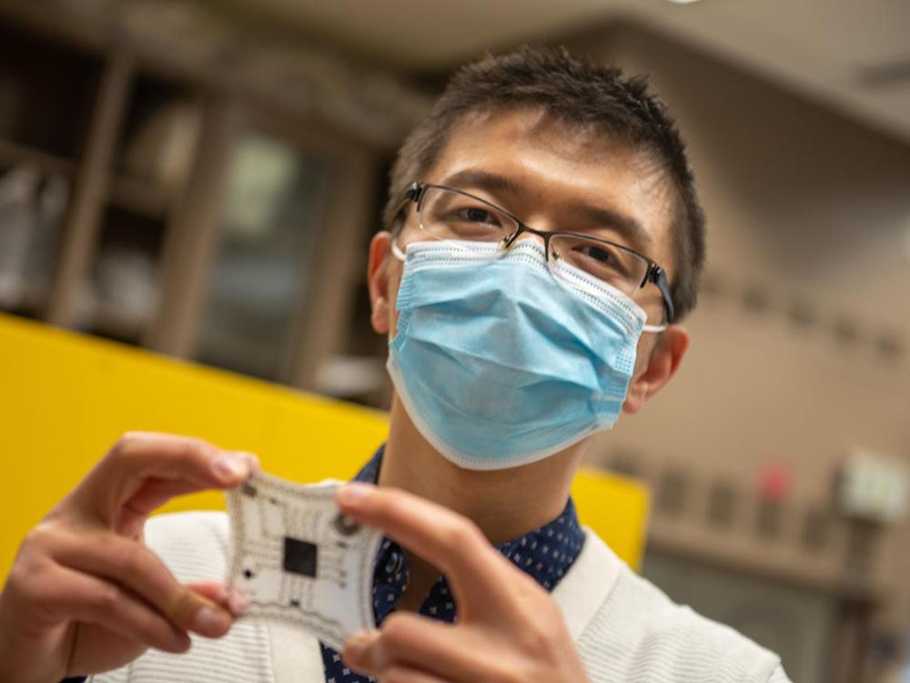 A man in a mask holds a medical device made of a flat, stretchy material and a metallic sensor