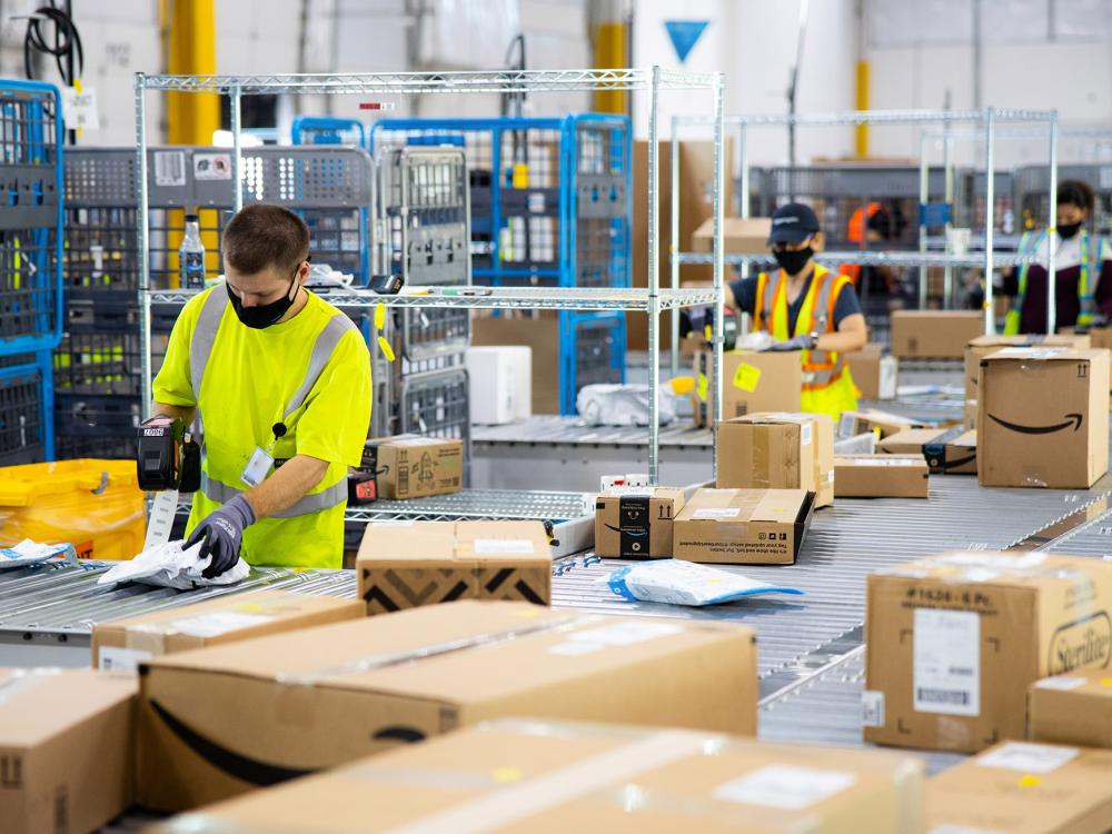 Amazon employees wearing masks sort numerous packages at a fulfillment center.
