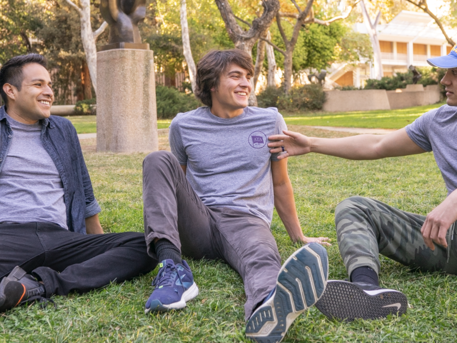 three fraternity members sitting in the grass