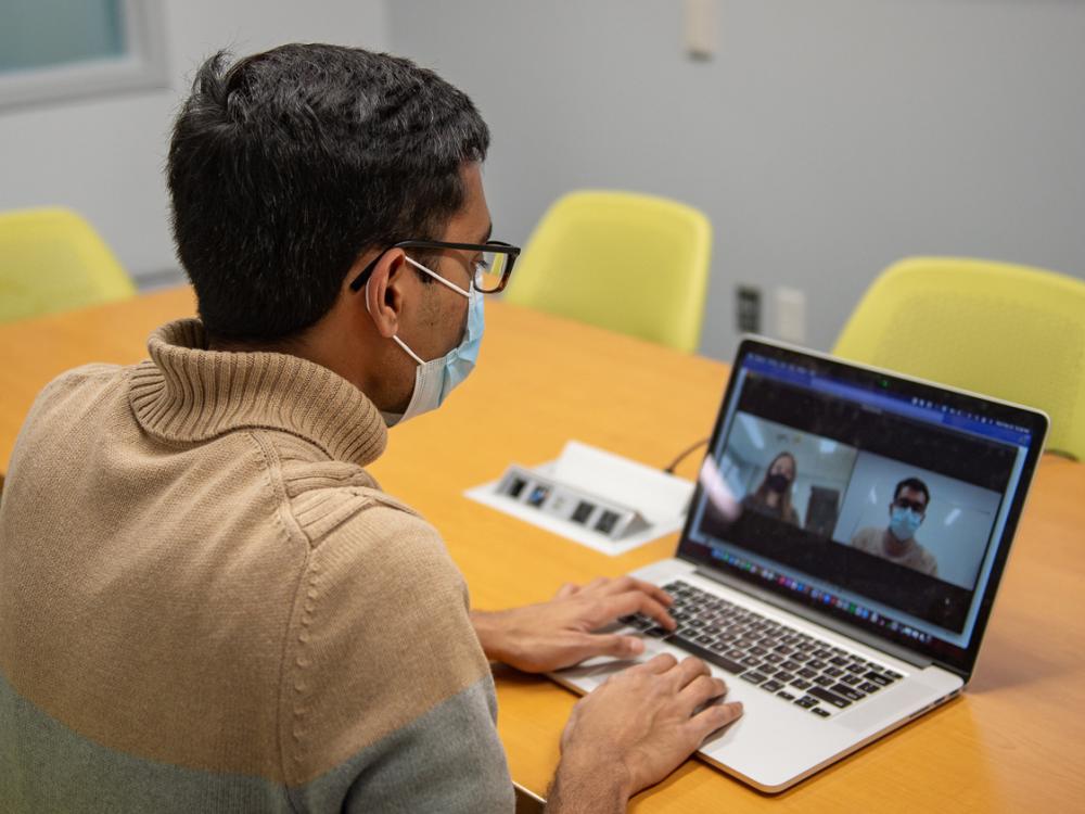 Researcher looking at a computer screen where a virtual meeting is taking place.