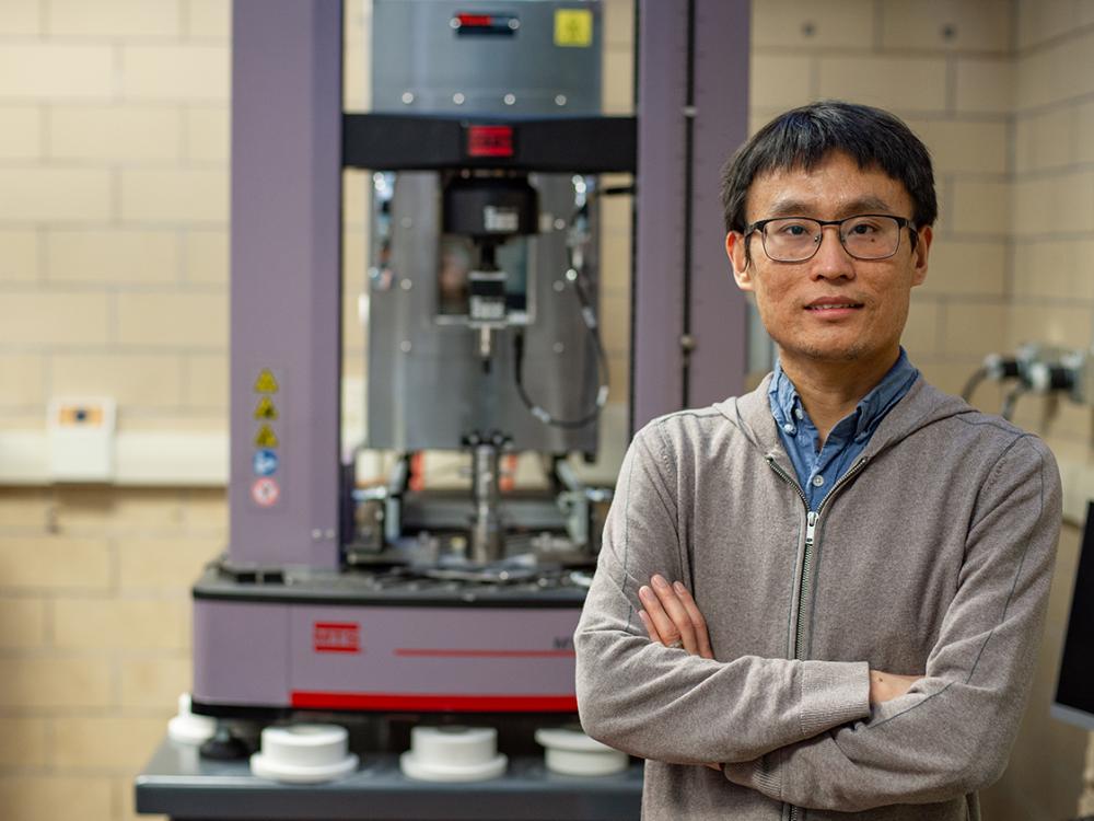 A man with arms crossed stands in front of a large piece of lab equipment. 