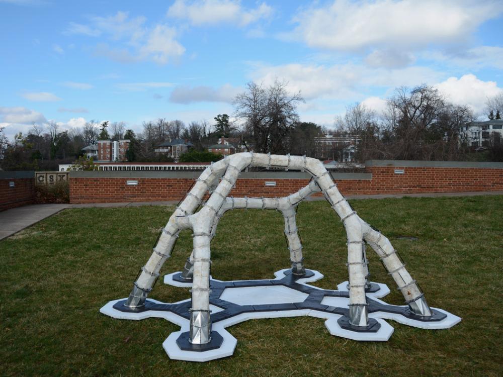A white architectural structure with six legs on a patch of grass. 