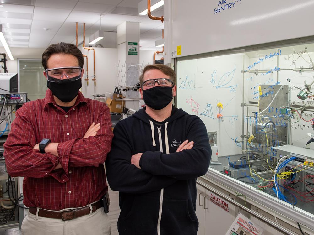 Two men with arms crossed stand in a lab.