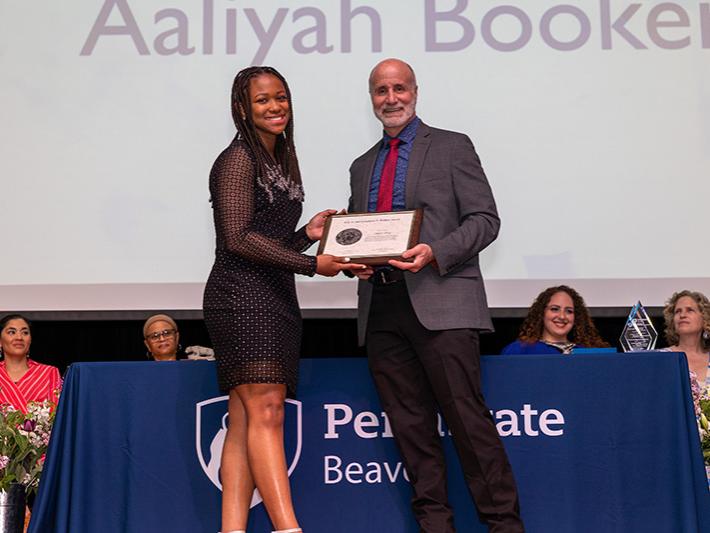 A female student is presented an award by campus staff member on stage